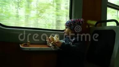 孩子在靠近窗户的火车上。 女孩吃馅饼，坐在火车上。